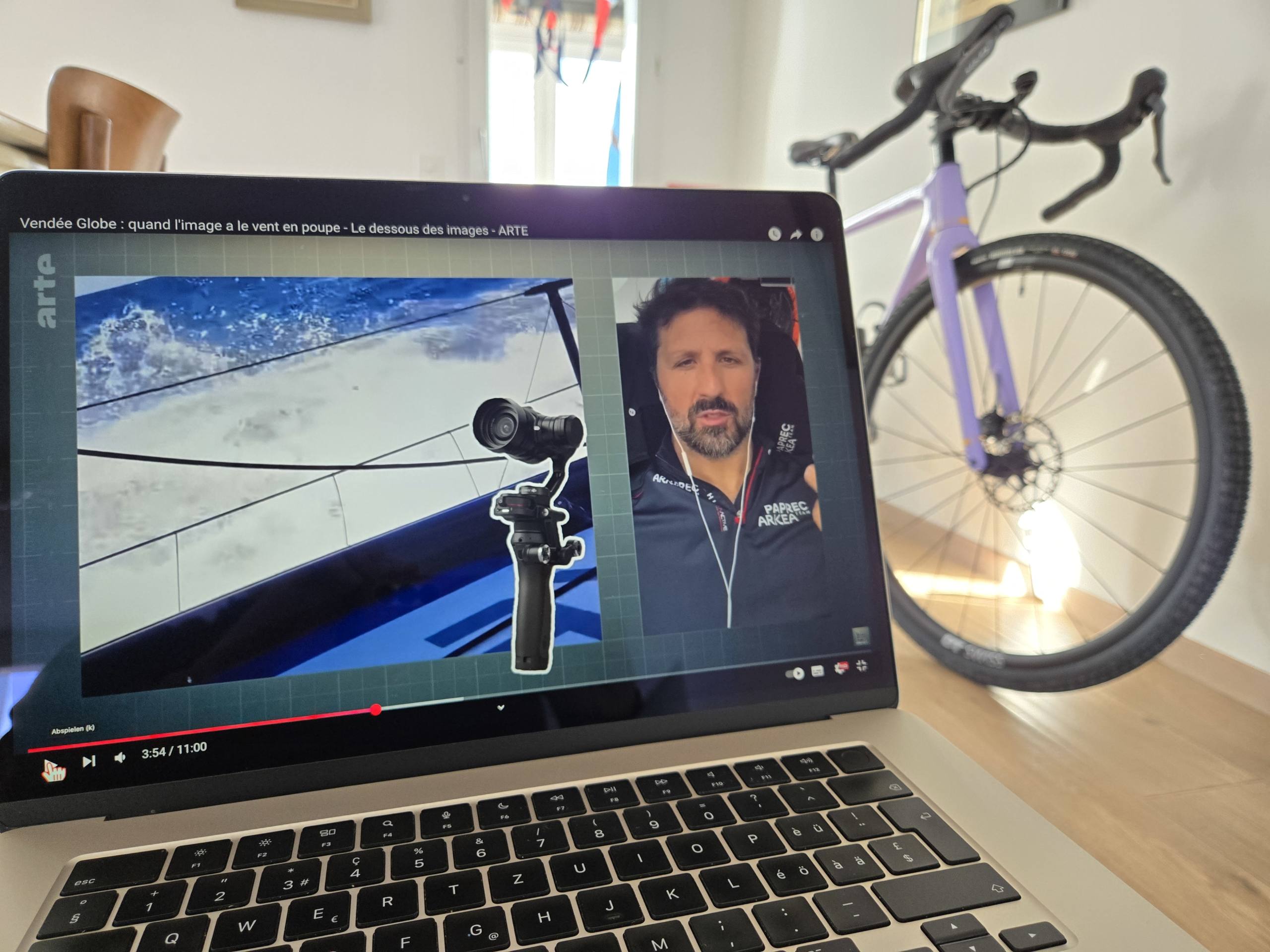 Ein Bild von einem Laptop, das ein YouTube-Video mit dem Titel «Vendée Globe: quand l'image a le vent en poupe - Le dessous des images - ARTE» zeigt. Das Video zeigt einen Skipper der erzählt, wie er als Medienschaffender unterwegs ist und mit welchen Mediengeräten, im Bild auch eine Kamera, die extra zur Herstellung von wackelfreien Videos dient.